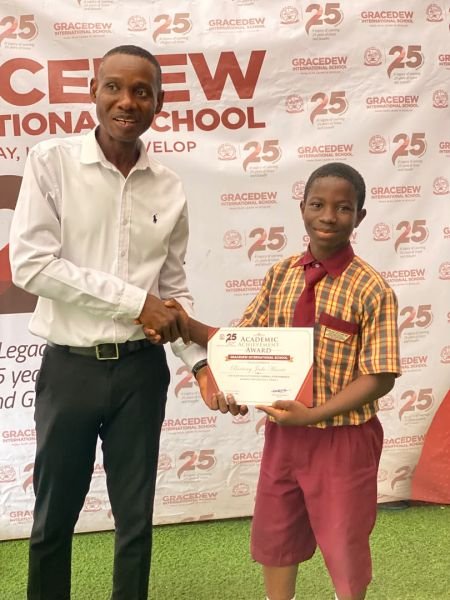 A Gracedew student being presented an award in front of the 25th anniversary backdrop