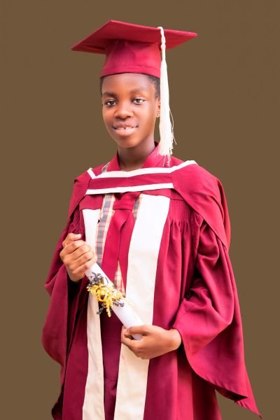 A Gracedew graduate in maroon cap and gown holding her certificate